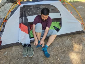 Putting on toe socks beside a backpacking tent to help prevent hiking blisters